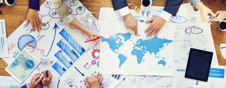 People around a table, photo is taken from above, they're looking at a map of the world